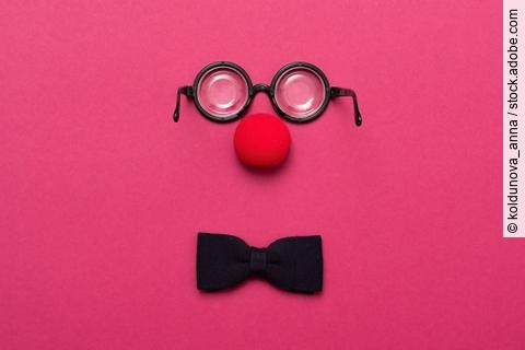 Eine Brille, eine rote Clownsnase und eine Schleife auf pinkem Hintergrund.