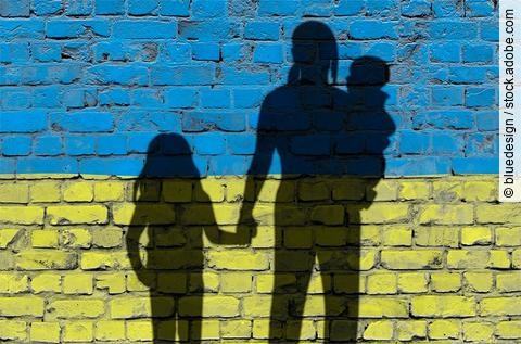 Flucht: Frauen und Kinder auf der Flucht; als Schatten vor einer Mauer in Ukrainefarben