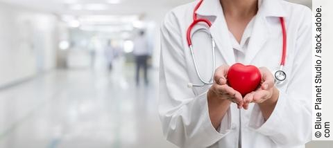 Ein Arzt hält eine rote Herzfigur in den Händen 