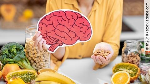 Frau hält ein aufgezeichnetes Gehirn und auf dem Tisch liegen Früchte und Nüsse.