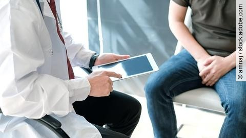 Arzt hält ein iPad und berät einen Patienten (beide sitzend).