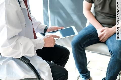 Arzt hält ein iPad und berät einen Patienten (beide sitzend).