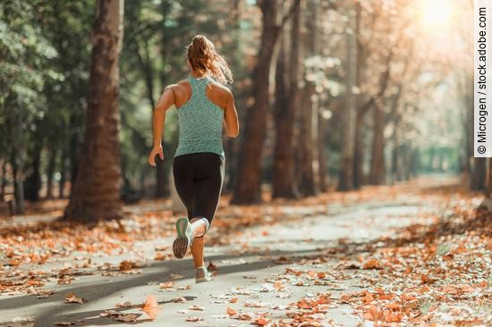 Frau joggt auf einem Waldweg im Herbst.