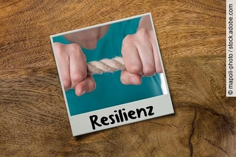 Bild ist mit dem Wort Resilienz beschriftet. Abgebildet ist eine Person, die ein Seil zwischen den Händen spannt.