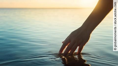 Eine weibliche Hand berührt die Wasseroberfläche von einem See.
