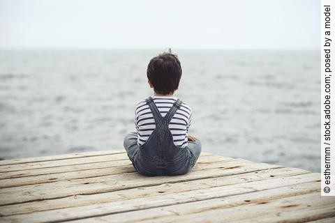 Kind sitzt im Schneidersitz und blickt auf das Meer.