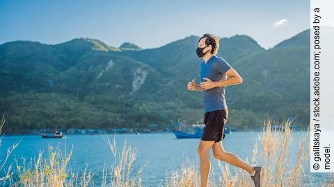 Ein Läufer mit FFP2-Maske joggt an einem Seeufer bei gutem Wetter.