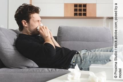 Mann mit Schnupfen liegt auf dem Sofa und putzt sich die Nase