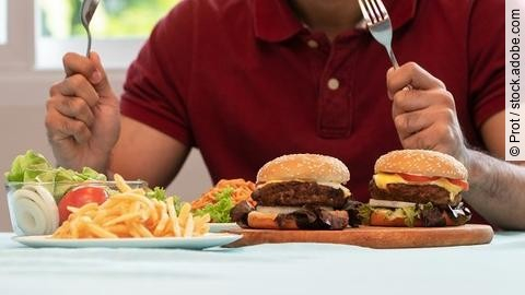 Mann mit Messer und Gabel am Tisch mit Burger, Pommes und Salat