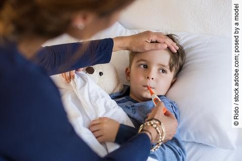 Kind mit Fieberthermometer und Teddy im Bett
