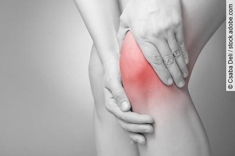 Schwarz-weiß Bild einer Person, die ihr schmerzendes Knie massiert.