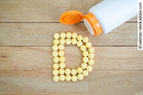 Gelbe Pillen formen den Buchstaben D auf hölzernem Hintergrund, oben im Bild liegt eine Medikamentendose.