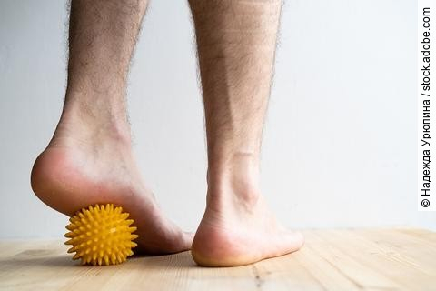 Füße, die über einen gelben Massageball mit Noppen rollen.