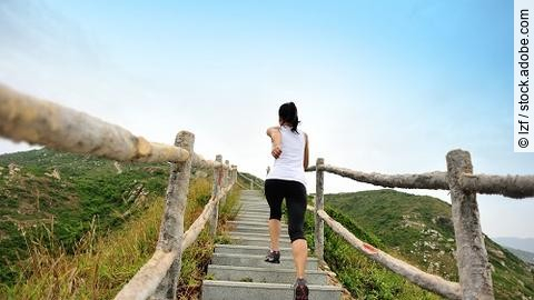 Frau rennt in Sportkleidung die Stufen an einem Berg hoch.