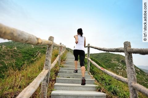 Frau rennt in Sportkleidung die Stufen an einem Berg hoch.