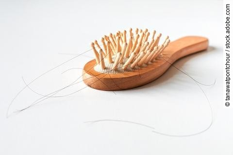 Haarbürste aus Holz mit ausgefallenen Haaren auf weißem Hintergrund