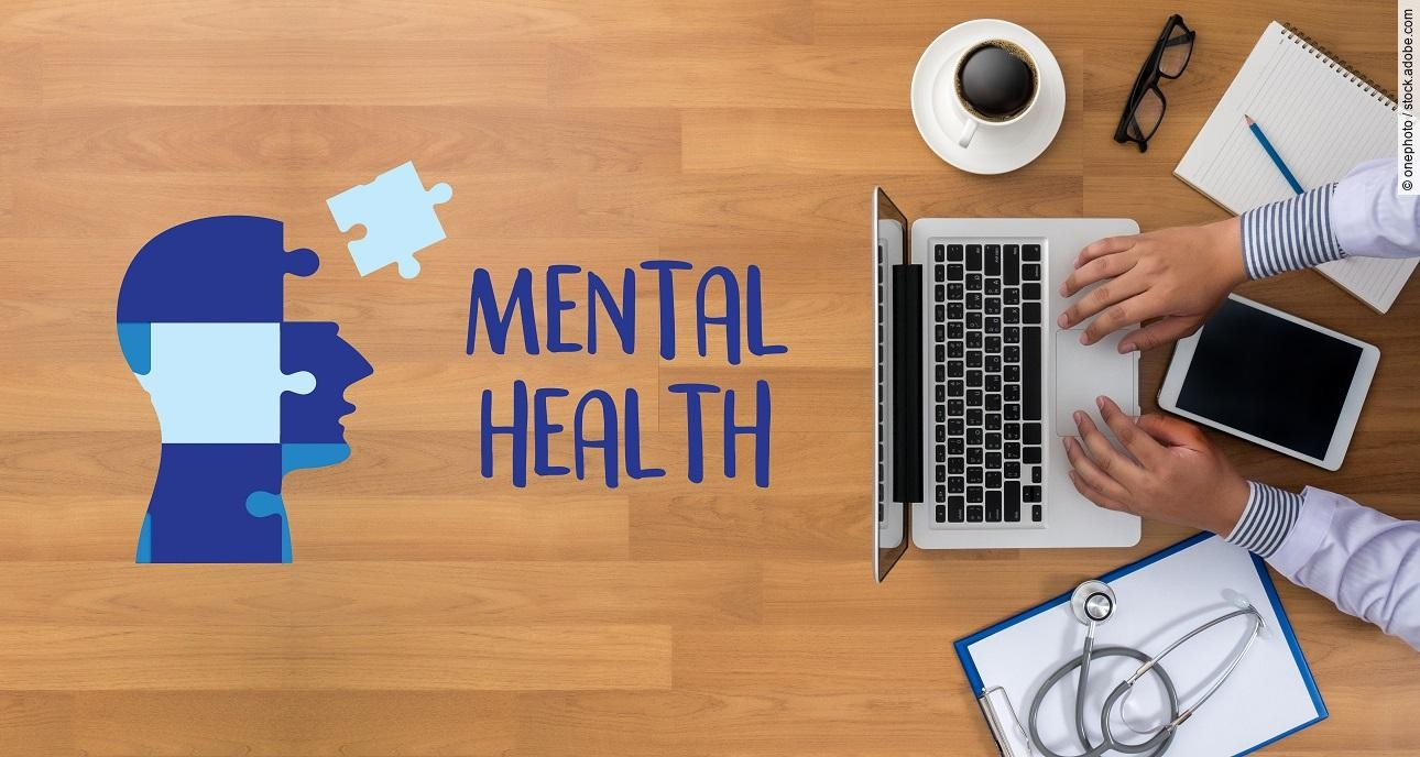 Umriss eines menschlichen Kopfs aus Puzzleteile, rechts daneben liegt ausgeschnitten das Wort mental health. Arzt sitzt am Tisch mit Arbeitsunterlagen.