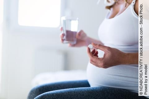 Schwangere Frau mit einem Glas Wasser und einer Tablette.